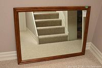 Large rectangular wall mirror leaning against a wall reflecting a carpeted stairway.