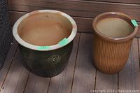 Photo showing both ceramic planters side by side on deck floor, green planter with floral motif and brown ribbed planter.