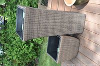 Two wicker outdoor planters on wooden deck, surrounded by garden greenery.