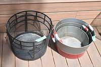 The photo shows a set of 3 metal nesting bins stacked inside each other next to a black metal mesh basket, both placed on outdoor wood planks.