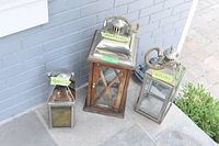All three outdoor lanterns placed side by side showing different sizes and materials (metal and wood). Each lantern has a rope handle and metal tops.