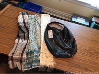 Four scarves laid out flat on a wooden table alongside a black leather purse.