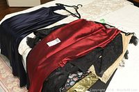 Pile of multiple evening dresses in navy, burgundy, black lace and gold fabrics laid out on bed