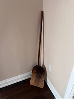 Full view of wooden grain shovel leaning against wall