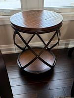 Full view of round accent table showing wood top, metal X braces, and lower shelf