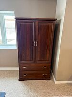 Front view of dark wood armoire showing paneled doors and two drawers