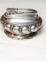 Front view of silver-plated tabletop lighter showing beaded design and flint wheel top