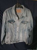 Front view of light blue denim trucker jacket on hanger