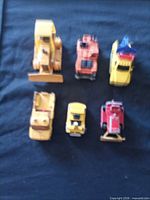 All six toy construction vehicles arranged two rows on dark surface, overall view