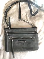 Front view showing grey faux suede bag, triple front zip pockets, chain/strap detail