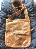 Front view of tan brown leather Roots messenger bag with embossed logo and adjustable strap