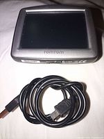 Front of TomTom ONE GPS with screen off and USB cable coiled