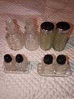 Group view showing two small shakers with black lids on matching tray plus other glass shakers in background