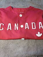 Folded red Canada jersey showing front buttons, lettering and maple leaf patch