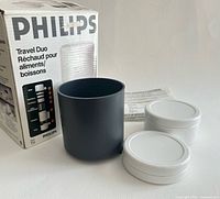 Box, black heating cup, two white containers and lids visible