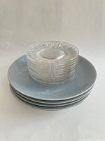 Stack of eight clear glass saucers atop four blue dinner plates