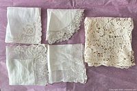 Five lace handkerchiefs and one cream lace doily displayed on tissue