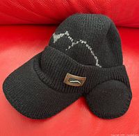 Black knit trapper hat front view showing visor, ear flaps and logo patch