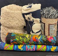 Group shot of five rolled textiles: two cat tapestries, beige plush throw, insect/hummingbird and safari animal wall hangings