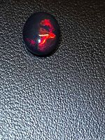 Loose oval cabochon opal showing red fire on dark background