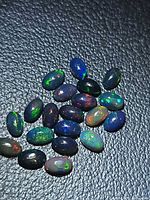 Group of approx 19 black opal cabochons on textured surface