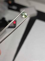 Sapphire held in tweezers showing oval shape and lagoon green-blue color