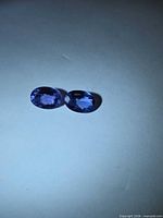 Two oval bluish-violet tanzanite stones on neutral background