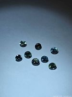 Eight round blue-green faceted sapphires on light background