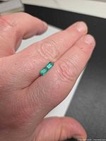 Pair of rectangular emerald cut green gemstones on fingertip