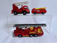 Three red die-cast fire trucks on acrylic riser