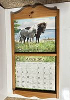 Front view of wooden calendar frame displaying March 2018 Lang calendar page with picture of two ponies