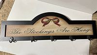 Front view of wooden stocking holder sign showing printed text, bow graphic, five metal hooks