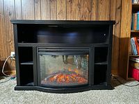 Front view of black electric fireplace console with curved glass front and side shelves