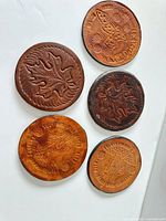 Five embossed leather coasters displayed face up on white surface