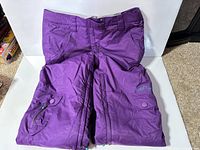 Front view purple Firefly snow pants folded, showing zip pocket and snap waistband