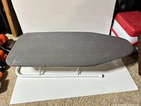Mini tabletop ironing board with gray cover and white metal foldable legs set on carpet