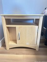 Front view of light wood night table showing open shelf, cabinet door with handle, arched base