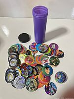 pile of assorted pogs and purple storage tube with cap