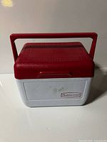 Front view of small Rubbermaid cooler with red lid and handle