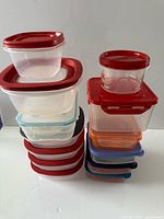 Two stacks of various size clear plastic containers with red, blue, orange, black lids