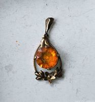 Front view of pendant showing orange glass stone, floral accent, bail