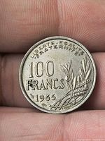 Reverse of 1955 100 Francs coin showing denomination, date, legend, olive and wheat sprigs