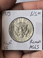 Reverse of 1973 Kennedy half dollar showing heraldic eagle in 2×2 holder with handwritten notes