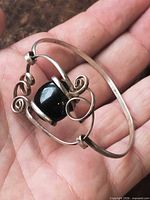 Bracelet held in hand showing scroll design and black bead