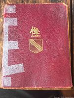 Front cover red leather with gilt crest, visible wear and taped spine
