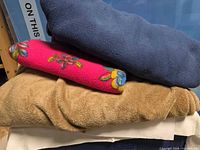 Stack showing navy fleece, pink embroidered fleece, tan fleece, off-white blanket