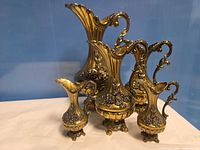 Front view of all five ornate brass pitchers