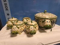 Front view of four lidded cow bowls, one open bowl, and lidded casserole in rack