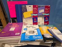 Group view of Avery label packs, Staples paper pack, Fellowes laminating pouches and blue binder