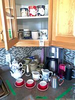 Overall countertop view with coffee maker, teapots, red cups, frothing pitcher and assorted items